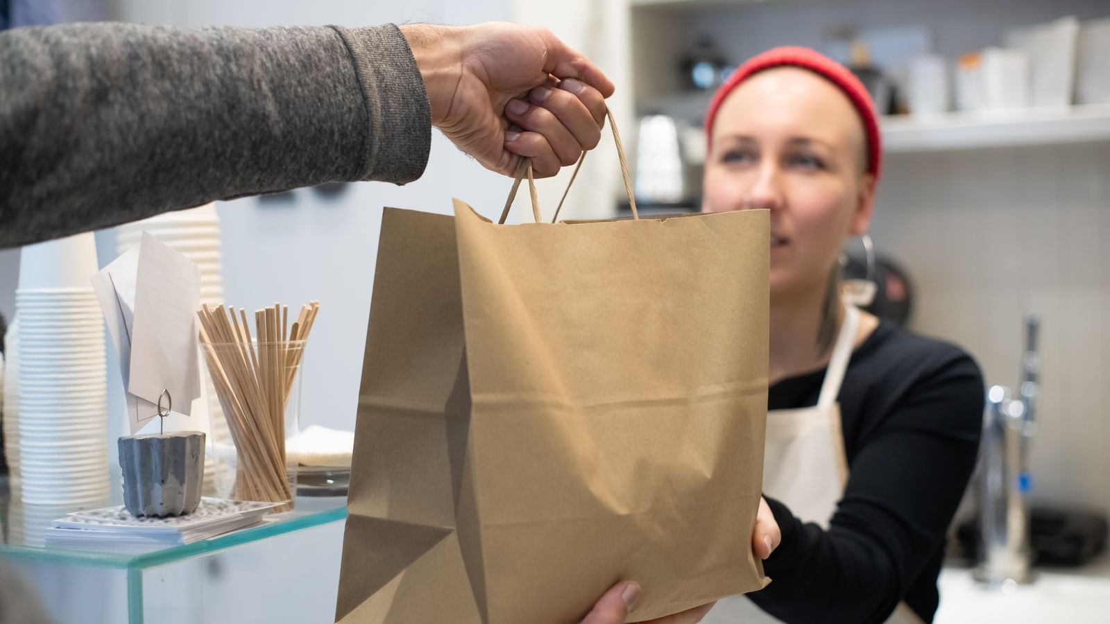Empleada de un local entregando una bolsa de papel con comida para llevar a un cliente